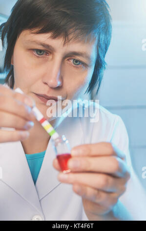 Portrait d'une femme scientifique en blouse blanche d'un pH tests échantillon liquide rouge Banque D'Images