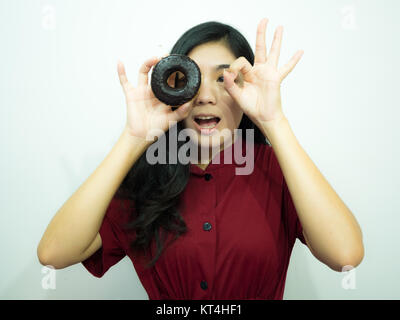 Asian woman holding donut sur fond blanc, chemise rouge, de longs cheveux noirs Banque D'Images