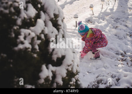 Un bébé fille portant un manteau coloré joue dans la neige. Banque D'Images