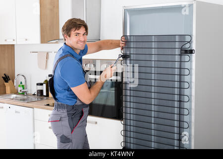 Conscrit travaille sur un réfrigérateur à l'aide d'un tournevis Banque D'Images