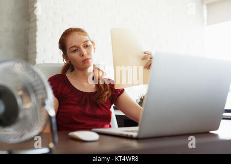 Portrait de jeune femme rousse travaillant avec l'ordinateur portable en fonction à l'été pendant la canicule. La température est chaude et le conditionneur de cheveux est b Banque D'Images