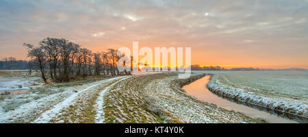 Rivière sinueuse dans un paysage de prairie gelé tôt le matin avec le soleil levant sous ciel magnifique Banque D'Images