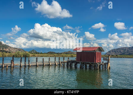 Une cabane sur l'extrémité d'une jetée en bois sur un lac avec des roseaux verts sous un ciel bleu avec des nuages blancs Banque D'Images