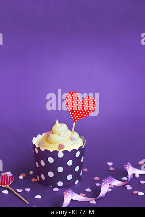 Cupcake à la vanille avec des petits coeurs décoratifs et coeur rouge en duvet, en violet papier cuisson cup, contre fond violet Cupcake pour la Saint-Valentin w Banque D'Images