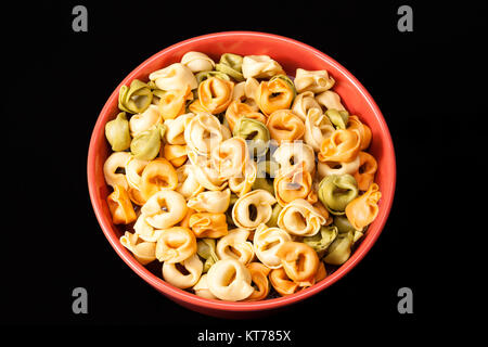 Tortellini de couleur en forme d'anneau, les pâtes dans un bol rouge Banque D'Images