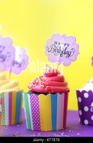 De savoureux petits gâteaux aux fraises dans les moules de papier coloré, avec Joyeux Anniversaire carte de vœux, sur fond jaune. Party background Banque D'Images