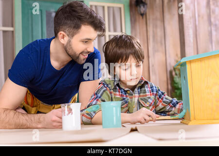 Heureux père à peu concentré au fils peinture wooden birdhouse on table Banque D'Images