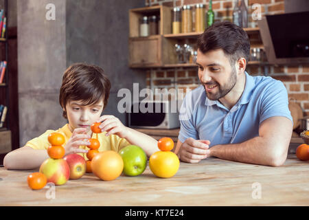 Heureux père et fils jouant avec les agrumes à table de cuisine Banque D'Images