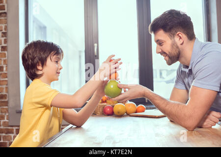 Vue latérale d'heureux père et fils jouant avec les agrumes dans la cuisine Banque D'Images
