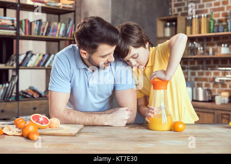 Père et fils presser le jus d'orange frais à table de cuisine Banque D'Images