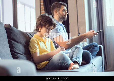 Père regarder la vidéo et prendre le petit déjeuner tout en fils faire leurs devoirs Banque D'Images