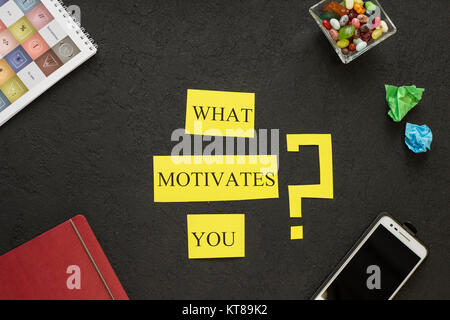 Qu'est-ce qui vous motive question imprimé sur un carton jaune dans un cadre d'articles de bureau. Arrière-plan de béton noir. Concept d'affaires et de gestion. L'espace pour votre Banque D'Images
