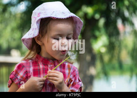 Petite fille dans un chapeau soufflé un pissenlit Banque D'Images