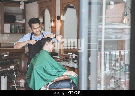 Cheerful young man getting haircut par coiffure à barbershop Banque D'Images