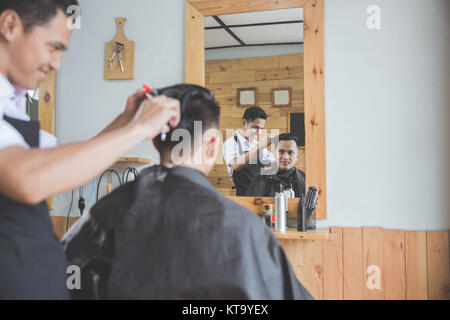 Cheerful young man getting haircut par coiffure à barbershop Banque D'Images