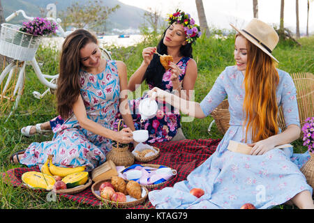 De belles femmes dans de longues robes profiter de pique-nique, s'amuser, verser le thé, manger un croissant. Palmiers et location on background Banque D'Images