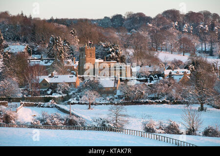 L'église Saint Laurent à Bourton On The Hill dans la neige au lever du soleil en décembre. Kingham Hill, Cotswolds, Gloucestershire, Angleterre. Banque D'Images