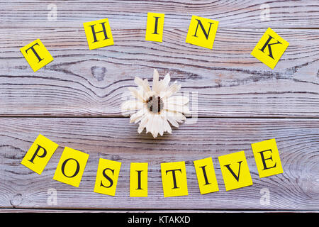 Pensez positif inscription imprimé sur papier jaune avec une fleur au milieu, vue du dessus.Light fond de bois. La motivation et l'entreprise concept. Sp Banque D'Images