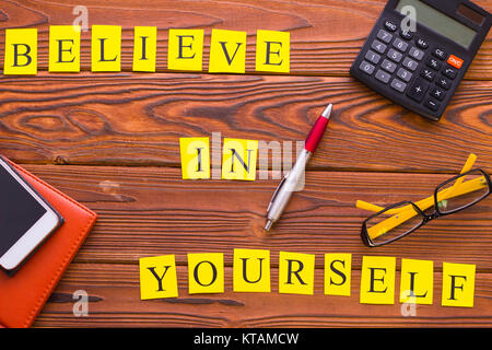 Croyez en vous-même l'inscription imprimée avec les fournitures de bureau, vue d'en haut. Rustique en arrière-plan. La motivation et l'entreprise concept. L'espace pour votre texte Banque D'Images
