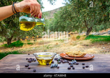 Verser la bouteille d'huile d'olive extra vierge de Crète dans un bol sur la table en bois à un champ d'oliviers, la Grèce. Banque D'Images