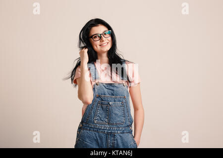 Beautiful smiling brunette girl wearing glasses en posant l'ensemble denim à côté de mur vierge Banque D'Images