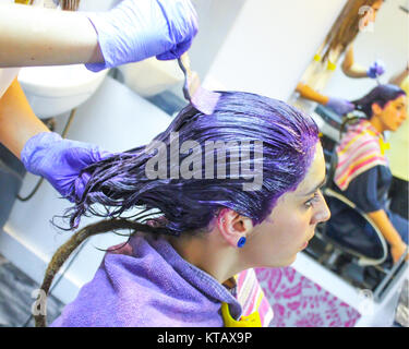 Jeune femme cheveux coloration lilas dans le salon de coiffure à l'aide d'une serviette. Elle a une longue tresse rasta c'est ; non peinte est assis en face du miroir Banque D'Images