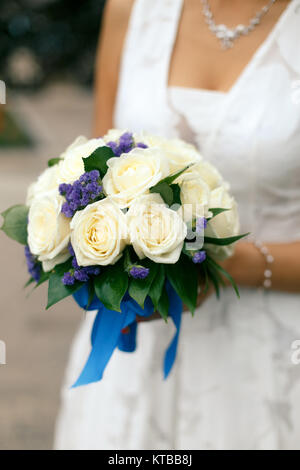 Bride holding bouquet de mariage des roses crème et fleurs violettes avec un ruban bleu Banque D'Images