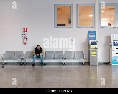 Biella, Italie - 15 décembre 2017 : Seul homme attend assise dans l'atrium de l'hôpital près de Biella le rapport des machines. Moment de la vie réelle pendant que vous Banque D'Images