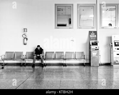 Biella, Italie - 15 décembre 2017 : Seul homme attend assise dans l'atrium de l'hôpital près de Biella le rapport des machines. Moment de la vie réelle pendant que vous Banque D'Images