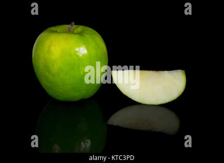 Green Apple entières ou coupées en tranches sur le dessus d'une surface en verre réfléchissant, fond noir Banque D'Images