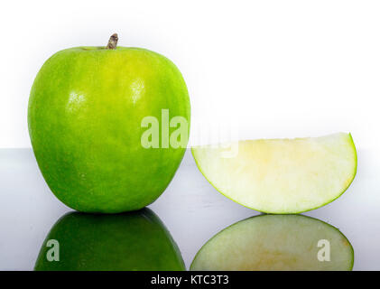 Green Apple entières ou coupées en tranches sur le dessus d'une surface en verre réfléchissant, fond blanc Banque D'Images