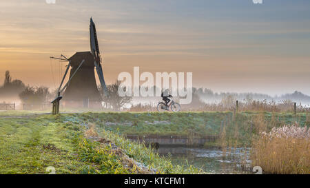 Cycliste de tôt le matin brumeux paysage avec moulin à vent en bois historique Banque D'Images