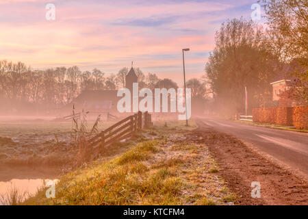 Misty street in dutch village rural sur la campagne avec église en early morning light rose coloré Banque D'Images