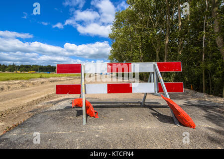 Le rouge et blanc aucune barrière d'entrée sur une petite route de campagne asphaltée Banque D'Images