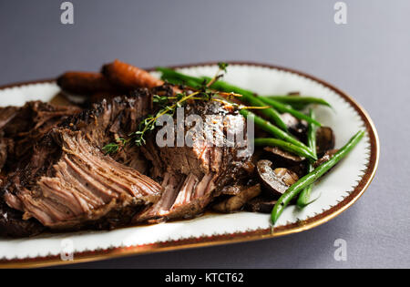 De mijotés avec les haricots verts, les carottes et les champignons sur une assiette blanche. Nappe grise, garnir de thym. Copier l'espace. Banque D'Images