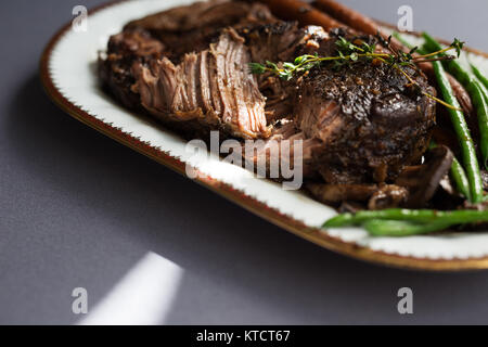 De mijotés avec les haricots verts, les carottes et les champignons sur une assiette blanche. Nappe grise, garnir de thym. Copier l'espace. Banque D'Images