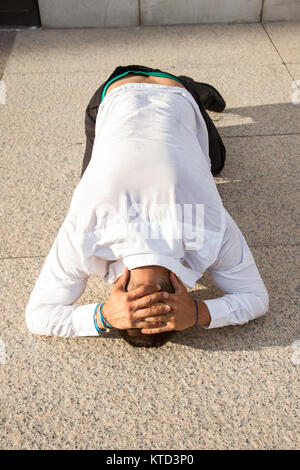 Beau, blanc et solide homme posant dans la rue. Il est couché sur le sol avec ses mains sur la tête de désespoir. Banque D'Images