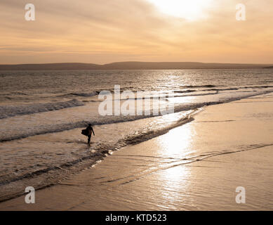 Un surfeur en silhouette portant un surf sortant de la mer Banque D'Images