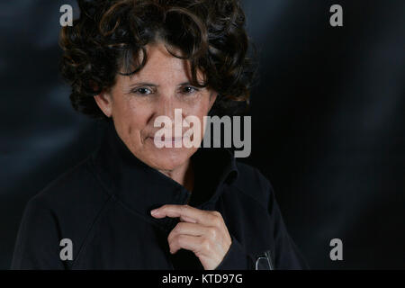 Femme d'âge moyen avec des cheveux bruns bouclés smiling en pensée, collier holding sur la veste et lunettes de lecture isolated on black Banque D'Images