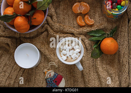 Une tasse de café aromatique avec de la guimauve, mandarines mûres, une bougie, une décoration d'un arbre de Noël sous la forme d'un bonhomme et un pot. Banque D'Images