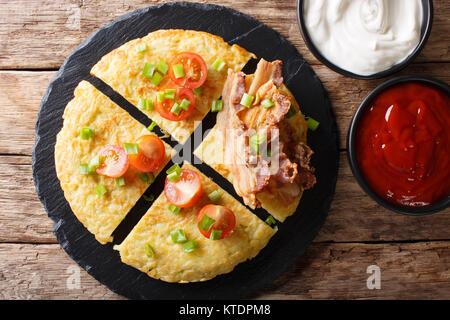 Galettes de pommes de terre avec du bacon, des tomates, des oignons et les sauces close-up sur une plaque horizontale de haut. abovel Banque D'Images