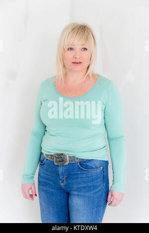 Femme blonde en vert et bleu jeans debout sur son genou à l'intérieur de salle vide Banque D'Images