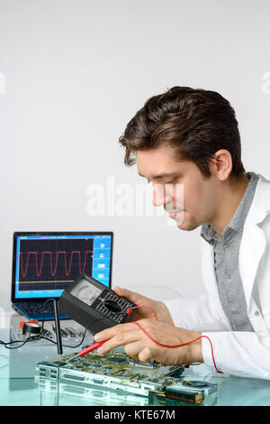 Jeune homme énergique tech ou réparations ingénieur équipement électronique. Shallow DOF, se concentrer sur la main de devant et le visage du travailleur. Banque D'Images