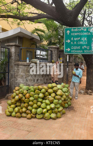 Un vendeur de rue, debout près de tas de coco tout en vendant au client dans la rue, signe de l'information en arrière-plan à Bangalore, Bangalore, Karnat Banque D'Images