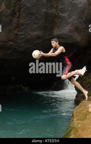 Jeune adulte Jeune Indien sauter d'une petite falaise en frais de bleu piscine de l'eau, tenant une balle sur un Nagarmadi Chendia, chutes d'eau, Karnataka, Inde. Banque D'Images