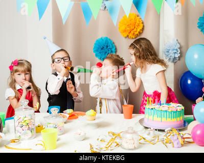 Groupe d'enfants souriants jouant sur l'anniversaire à décorée. Happy kids soufflé dans les tuyaux sur Birthday party Banque D'Images