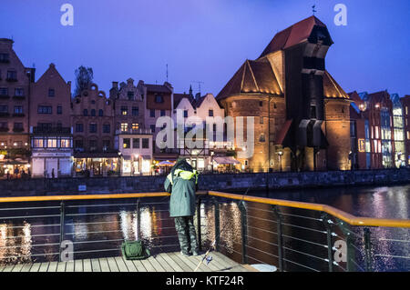 Pêche à l'homme à la rivière Motlawa par nuit en face de la grue médiévale. Gdansk, Pologne Banque D'Images