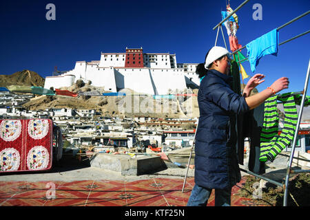 Femme tibétaine faisant la blanchisserie à toit plat avec l'Samdruptse Dzong en arrière-plan. Shigatse, Tibet Banque D'Images