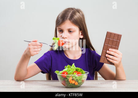 Petite fille est malheureuse car elle n'aime pas manger de la salade. Elle préfère le chocolat. Banque D'Images