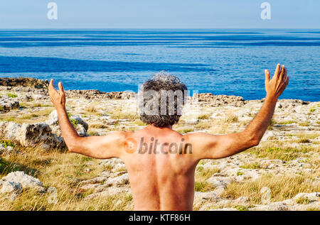 Tatoo de domaine public logo bitcoin sur le dos de l'homme sensibiliser les mains tout en regardant vers l'horizon de la mer Banque D'Images